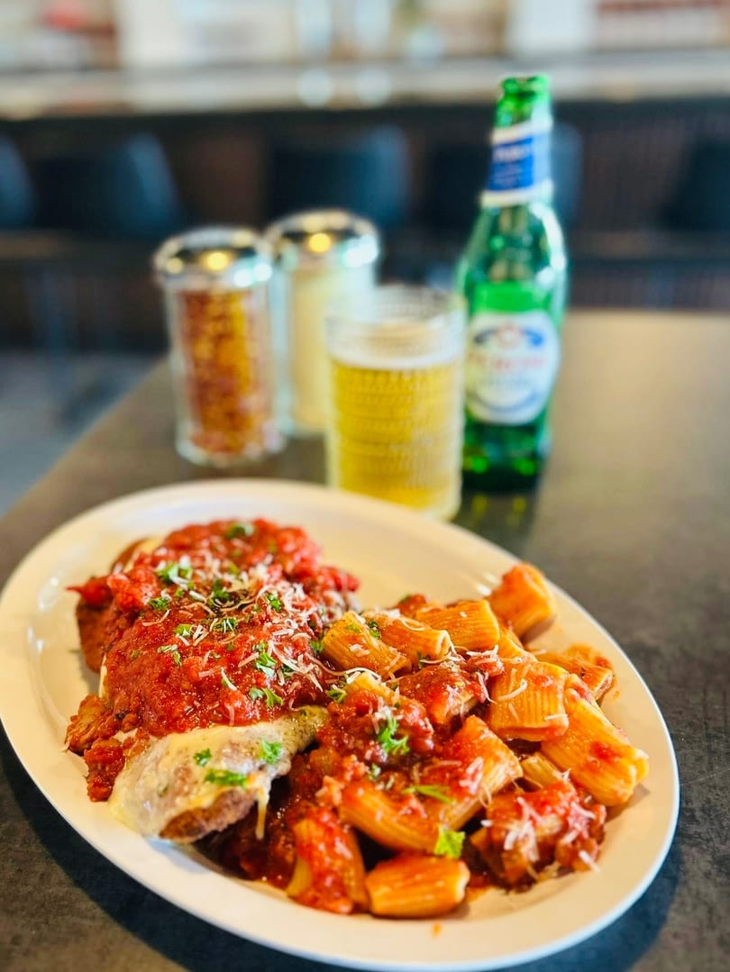 Chicken parmesan and rigatoni pasta with red sauce, cheese, and parsley, with beer.