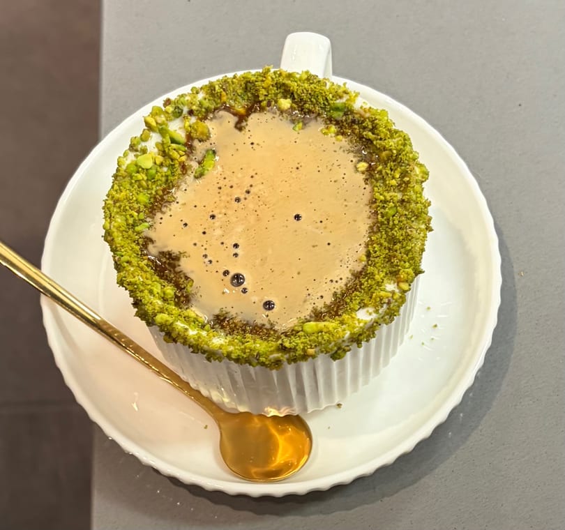 Overhead view of a coffee drink with a pistachio-crusted rim, served with a gold spoon.