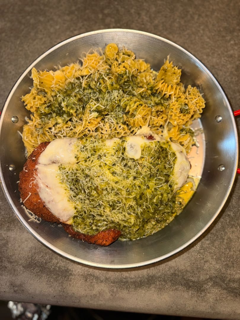 Chicken parmesan with pesto and pasta in a metal pan, topped with melted cheese.